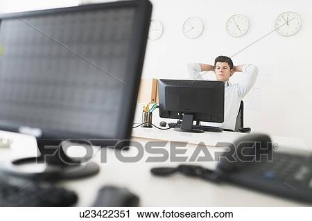 Stock Image - Young man sitting in front of desk and working. Fotosearch