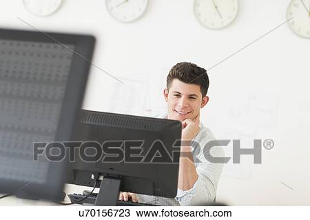 Young man sitting in front of desk and working View Large Photo Image Stock Image - Young man sitting in front of desk and working. Fotosearch
