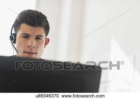 Stock Image - Young man sitting in front of desk and talking. Fotosearch