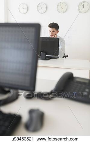 Young man sitting in front of desk and working View Large Photo Image Stock Image - Young man sitting in front of desk and working. Fotosearch