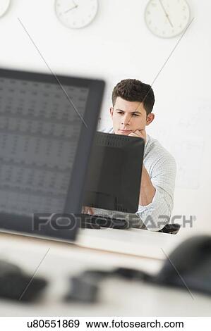 Stock Photo - Young man sitting in front of desk and working. Fotosearch