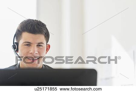 Stock Photography - Young man sitting in front of desk and talking. Fotosearch