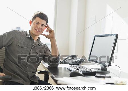 Stock Photograph - Young man sitting in front of desk. Fotosearch