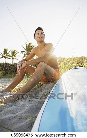 Young man sitting on beach with surfboard View Large Photo Image Stock Photography - Young man sitting on beach with surfboard. Fotosearch