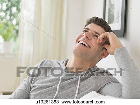 Young man sitting on sofa and smiling View Large Photo Image Stock Image - Young man sitting on sofa and smiling. Fotosearch