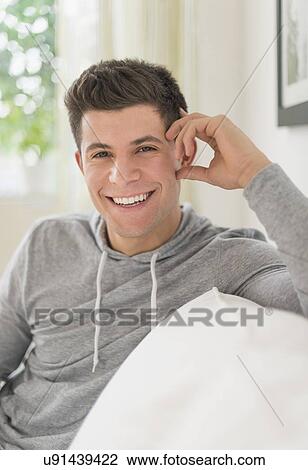Young man sitting on sofa and smiling View Large Photo Image Stock Image - Young man sitting on sofa and smiling. Fotosearch