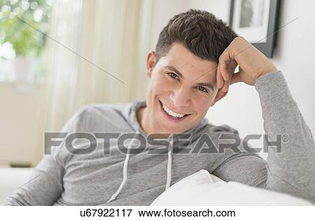 Young man sitting on sofa and smiling View Large Photo Image Stock Photo - Young man sitting on sofa and smiling. Fotosearch