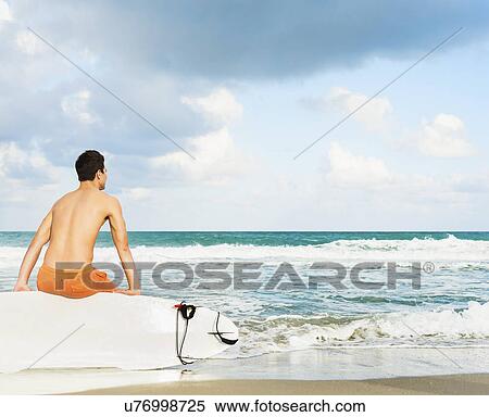 Stock Photography - Young man sitting on surfboard. Fotosearch