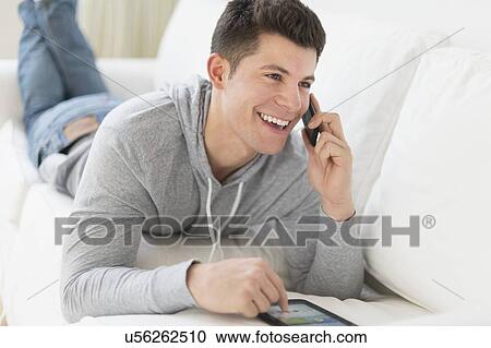 Young man using tablet and talking by phone View Large Photo Image Stock Image - Young man using tablet and talking by phone. Fotosearch