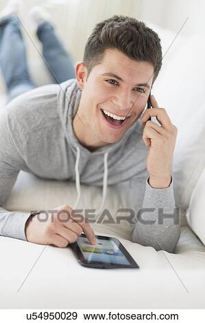 Stock Photo - Young man using tablet and talking by phone. Fotosearch