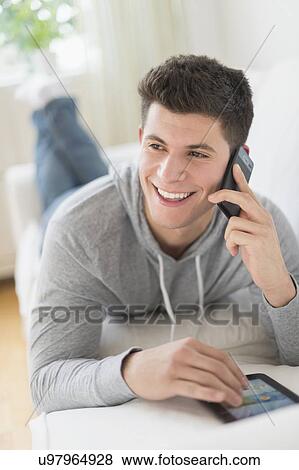 Stock Photo - Young man using tablet and talking by phone. Fotosearch