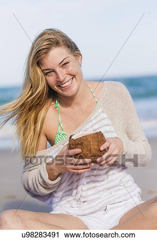 Stock Image - Young woman on beach drinking coconut juice. Fotosearch