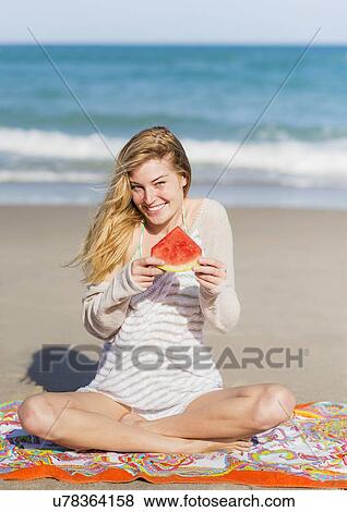 Stock Photo - Young woman on beach eating watermelon. Fotosearch