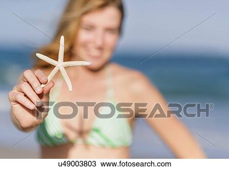 Stock Image - Young woman on beach holding starfish. Fotosearch
