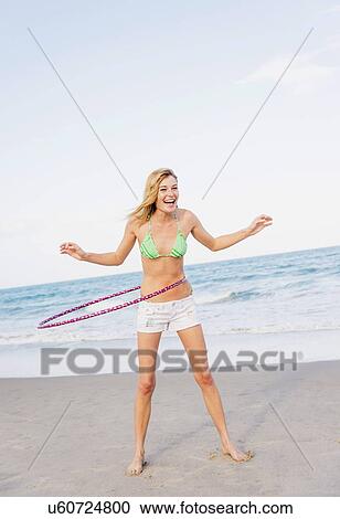 Stock Image - Young woman on beach twirling Hula hoop. Fotosearch