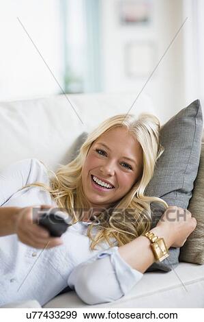 Stock Photo - Young woman watching tv on sofa. Fotosearch