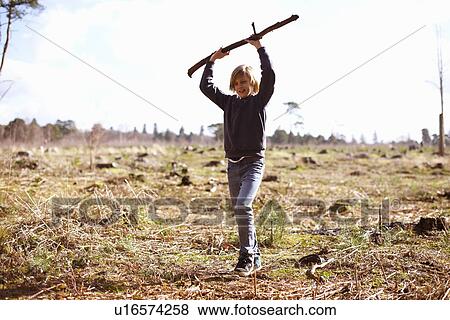 Boy holding up a stick in a plantation clearing View Large Photo Image Stock Photo - Boy holding up a stick in a plantation clearing. Fotosearch