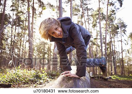 Stock Image - Boy jumping over a tree trunk in forest. Fotosearch