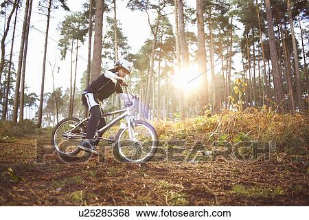 Stock Photo - Boy riding his BMX through forest. Fotosearch
