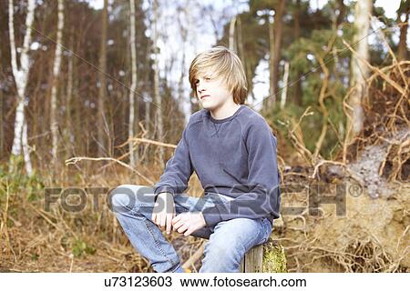 Stock Image - Boy sitting on tree stump in forest. Fotosearch
