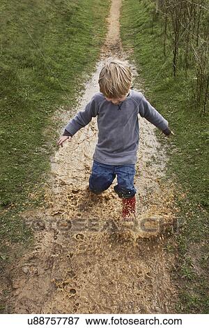 Stock Photo - Boy splashing through muddy puddle. Fotosearch