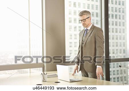 Businessman looking down at laptop on office desk View Large Photo Image Stock Image - Businessman looking down at laptop on office desk. Fotosearch