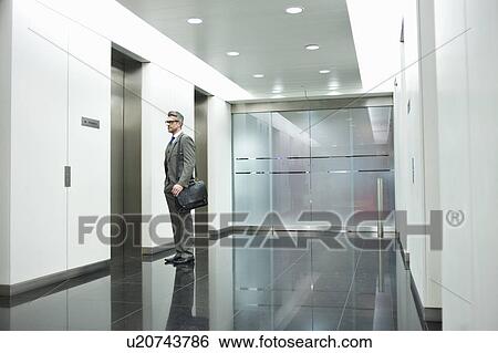 Stock Photograph - Businessman waiting for elevator in office corridor. Fotosearch
