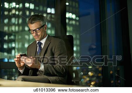 Businessman working late texting on smartphone View Large Photo Image Stock Photograph - Businessman working late texting on smartphone. Fotosearch