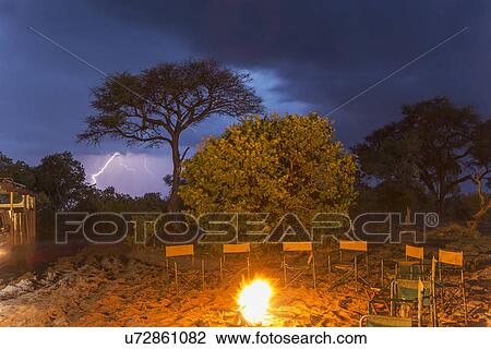 Stock Image - Campfire and a row of empty chairs at night, Kasane, Chobe National Park, Botswana, Africa. Fotosearch