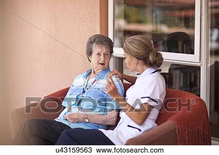 Stock Image - Care assistant chatting to senior woman on sofa. Fotosearch