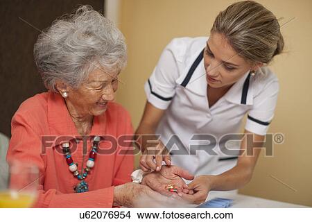 Picture - Care assistant handing medication to senior woman. Fotosearch