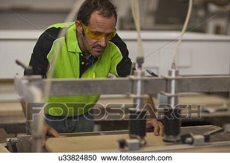Stock Image - Carpenter cutting wood on table saw in workshop. Fotosearch