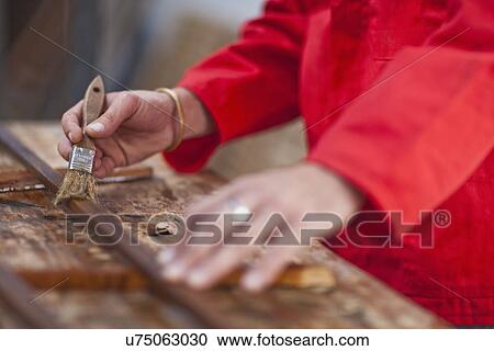 Stock Image - Carpenter varnishing wood, mid section. Fotosearch