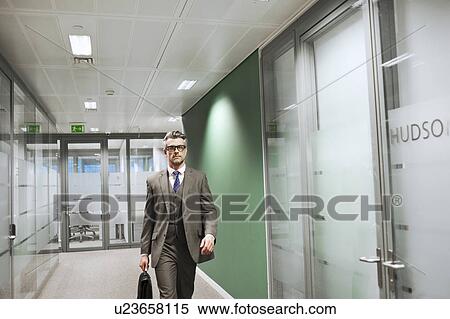 Stock Photography - Confident mature businessman walking along office corridor. Fotosearch