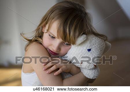 Stock Image - Distressed girl holding onto teddy bear. Fotosearch