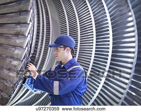 Stock Photo - Engineer inspecting repair to steam turbine blade in workshop. Fotosearch