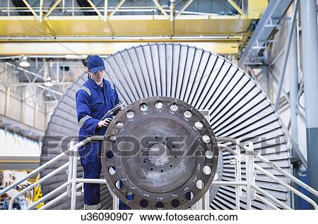 Stock Photo - Engineer inspecting turbine in workshop. Fotosearch