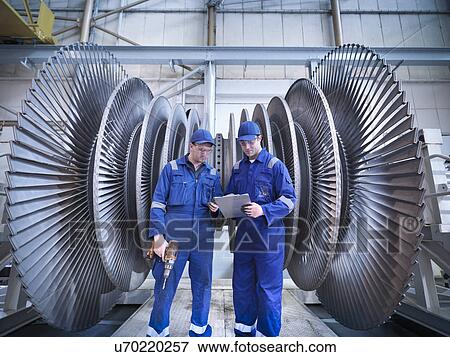 Stock Photo - Engineers discussing notes in front of steam turbine in workshop. Fotosearch