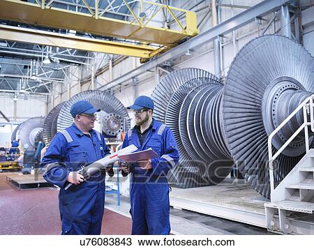 Stock Image - Engineers discussing rotor blade in turbine repair workshop. Fotosearch