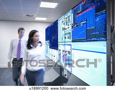 Stock Image - Financial analysts looking at screens in control room. Fotosearch