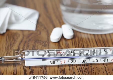 Stock Photograph - Galinstan thermometer showing elevated body temperature from fever, paracetamol pills, glass of water, tissue. Fotosearch
