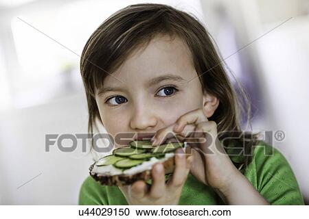 Stock Image - Girl eating a cheese and cucumber open sandwich. Fotosearch