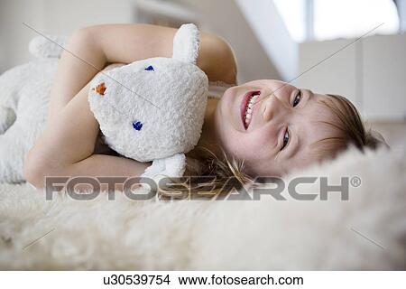 Picture - Girl lying on furry bed cuddling teddy bear. Fotosearch