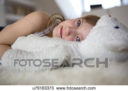 Stock Image - Girl lying on furry bed with teddy bear. Fotosearch
