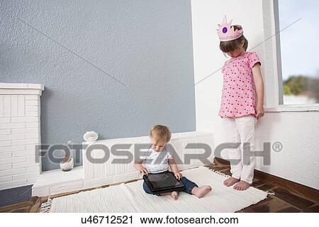 Stock Image - Girl watching over baby boy playing digital tablet. Fotosearch