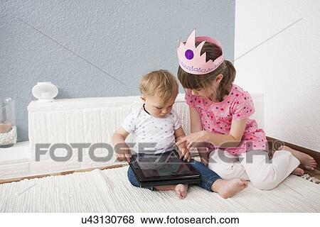 Girl watching over baby boy playing digital tablet View Large Photo Image Stock Photo - Girl watching over baby boy playing digital tablet. Fotosearch