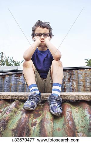 Stock Photo - Glum little boy sitting on roof. Fotosearch