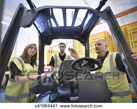 Stock Image - Instructor showing apprentices controls of forklift truck. Fotosearch
