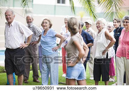 Stock Image - Large group of seniors exercising in retirement villa garden. Fotosearch