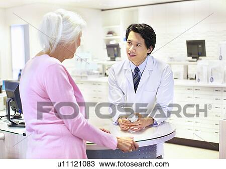 Stock Image - Male pharmacist advising customer on medication. Fotosearch